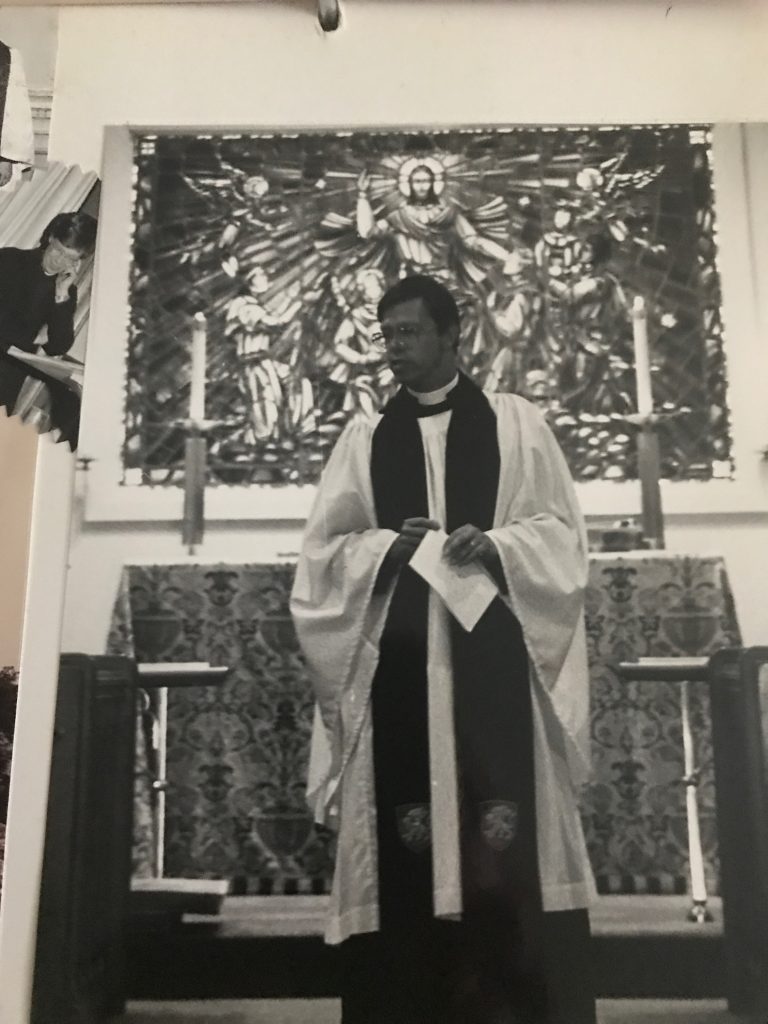 Vintage photo of priest standing in front of new stained-glass window with multicultural "angels" surrounding Christ